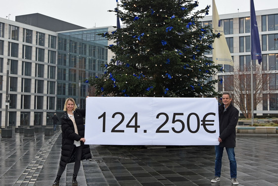 Die Mitarbeiterin der R+V STIFTUNG, Kristina Arndt, und Stiftungsleiter Ralph Glodek präsentieren das Rekordergebnis am Weihnachtsbaum auf dem Raiffeisenplatz vor der R+V-Zentrale in Wiesbaden.