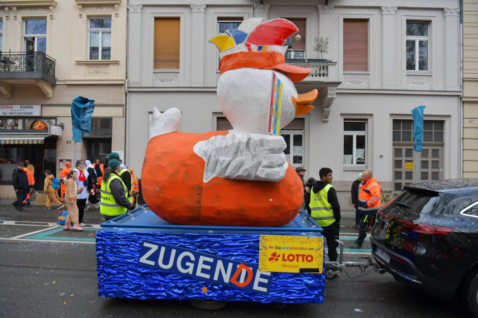 Es war eine Nachricht, die bei den Wiesbadener Wagenbauern einschlug wie eine Bombe: Mainz verbietet Wiesbaden die „Zugente“. Doch was als juristischer Angriff auf die Fastnachtstradition begann, wurde durch einen Geistesblitz im Westend zur Geburtsstunde einer neuen Legende. Wir erzählen die exklusive Geschichte, wie aus einer Ente eine Gans wurde – und warum die Mainzer sich damit ein echtes Eigentor geschossen haben.